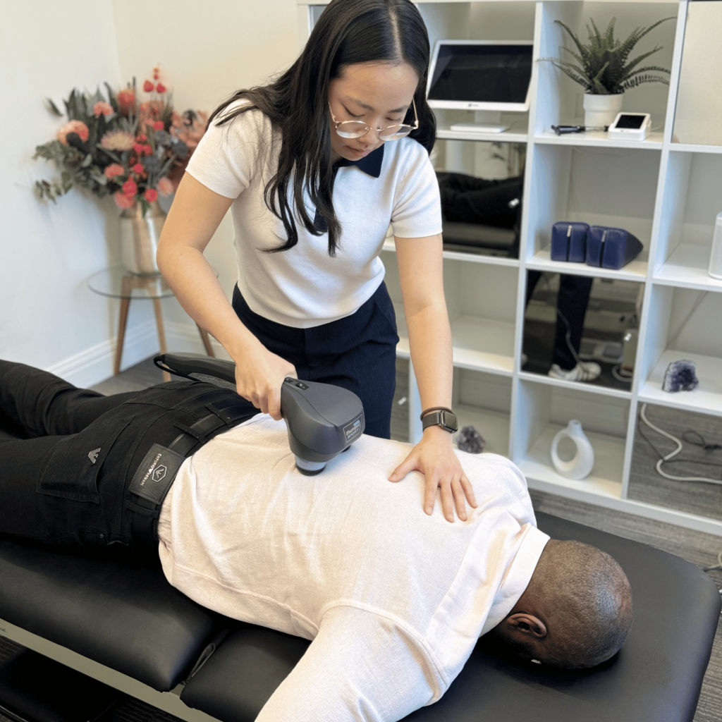 Physiotherapist using percussion therapy to relieve shoulder tension at Mayfair & Belgravia Chiropractic