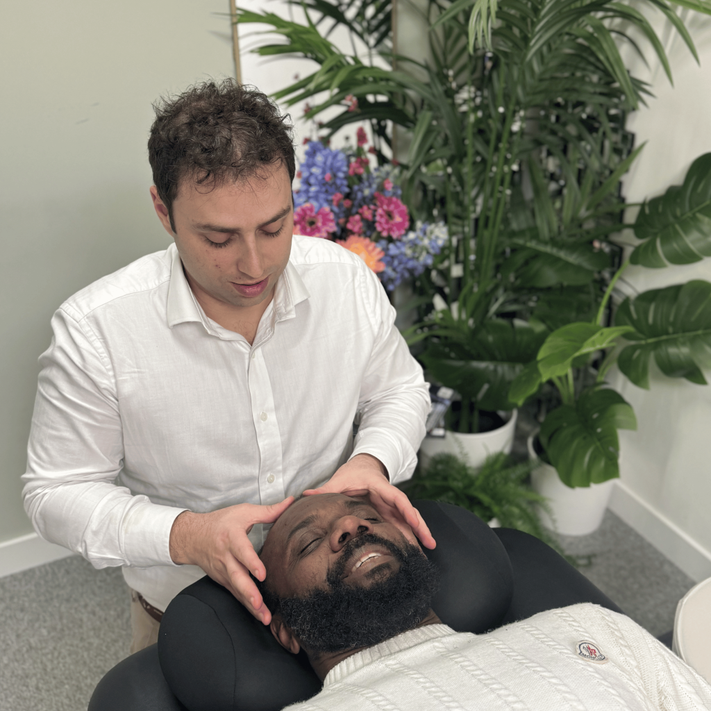 Chiropractor performing cranial therapy on a seated male patient at Mayfair & Belgravia Chiropractic